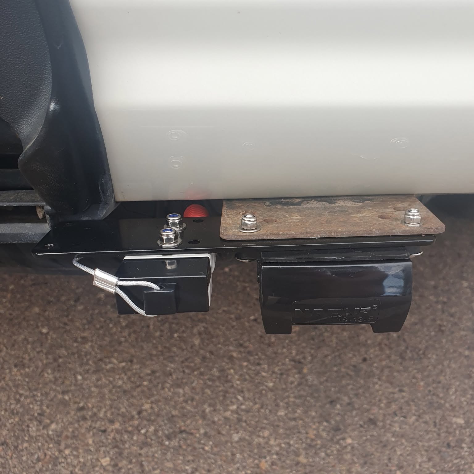 A trailer plug and connector bracket mounted under a vehicle tow bar with the breakaway cable attached