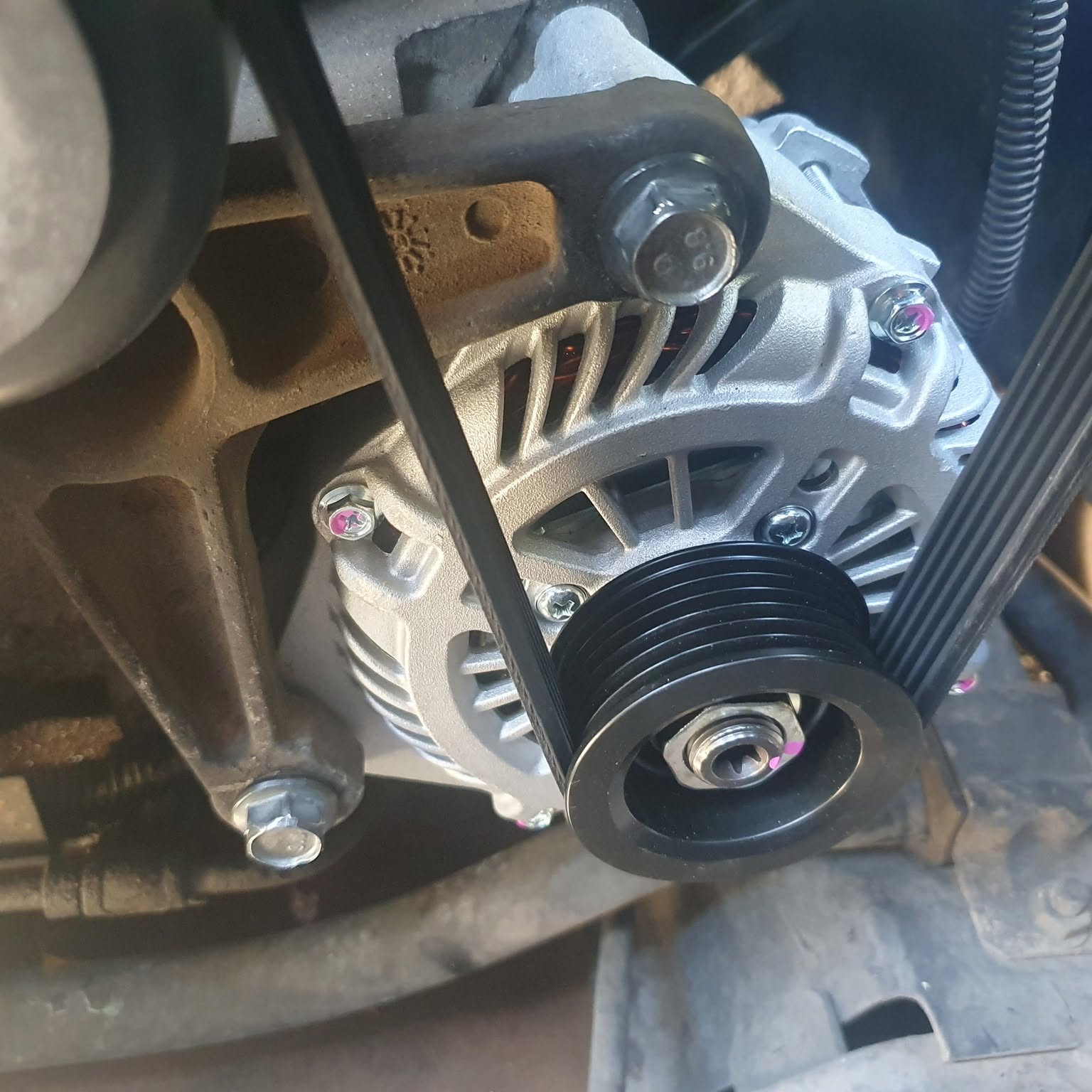 A newly fitted alternator in an engine bay with the drive belt tensioned over the pulley