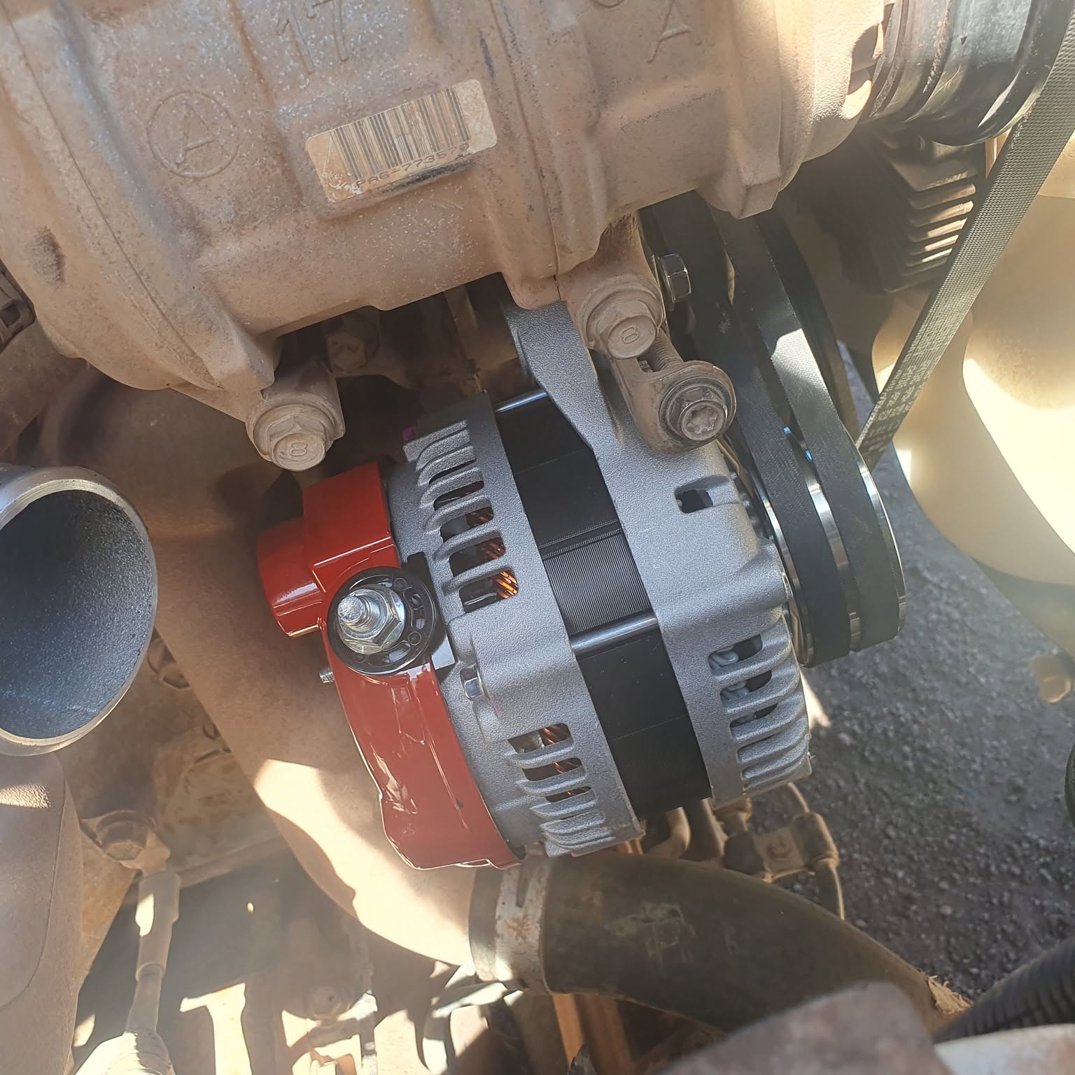 A high output alternator with a red end housing installed in a vehicle engine bay